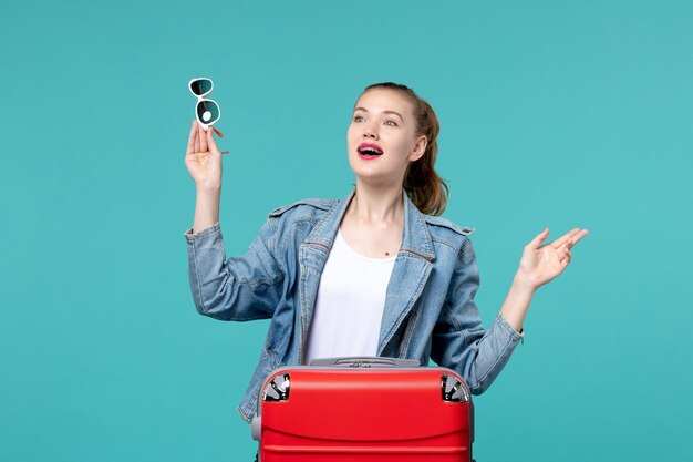 Vue de face jeune femme tenant des lunettes de soleil et se préparant pour des vacances sur l'espace bleu