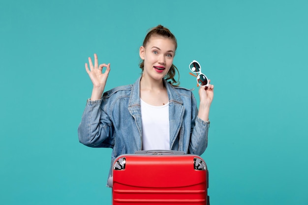 Vue de face jeune femme tenant des lunettes de soleil et se préparant pour des vacances sur l'espace bleu