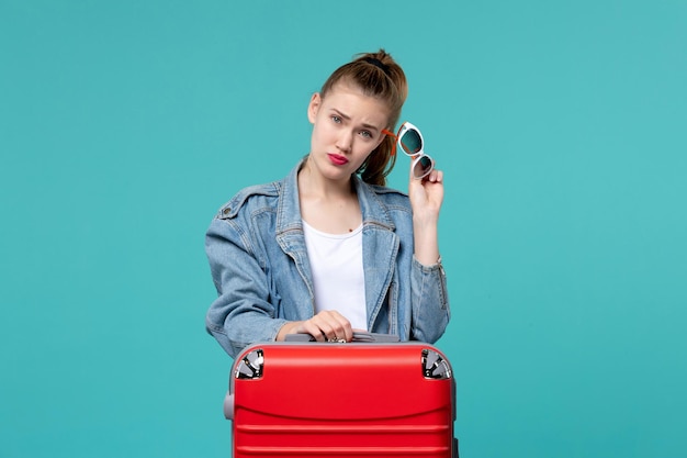 Vue de face jeune femme tenant des lunettes de soleil et se préparer pour les vacances sur le bureau bleu