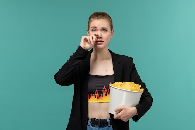 Vue de face jeune femme tenant et mangeant des chips en regardant un film sur un bureau bleu