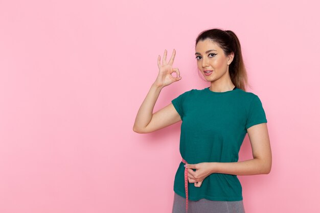 Vue de face jeune femme tenant la mesure de la taille sur le mur rose beauté sport exercice athlète séances d'entraînement slim