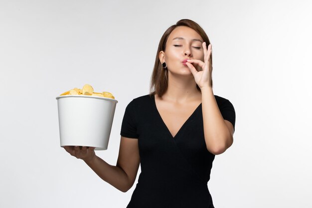 Vue de face jeune femme tenant le panier avec des croustilles et posant sur un bureau blanc clair