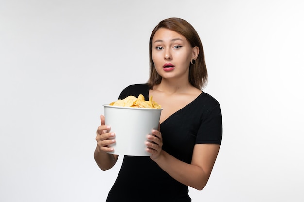 Vue de face jeune femme tenant le panier avec des croustilles et posant sur une surface blanche légère