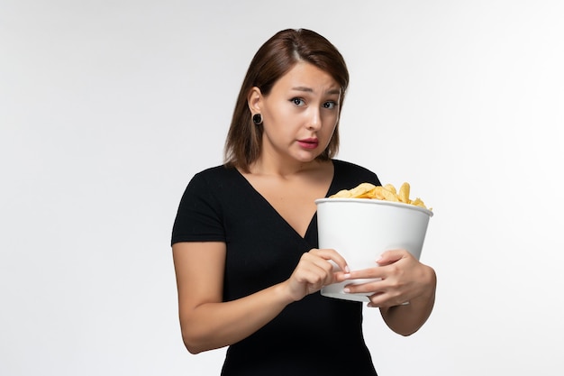 Vue de face jeune femme tenant le panier avec des croustilles regarder un film sur une surface blanche légère