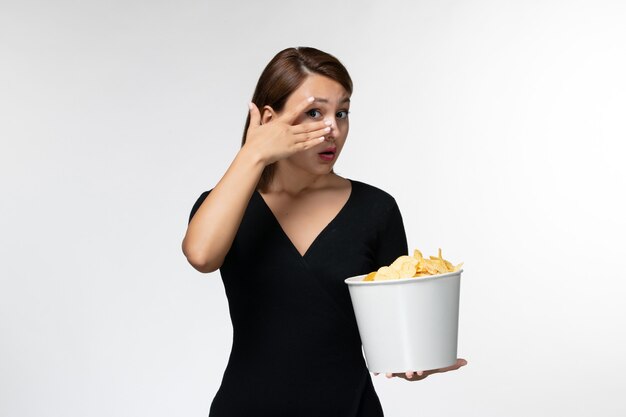 Vue de face jeune femme tenant le panier avec des croustilles regarder un film sur une surface blanche légère