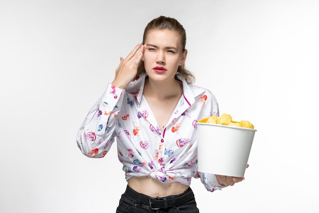 Vue de face jeune femme tenant le panier avec des croustilles regarder un film sur une surface blanche légère