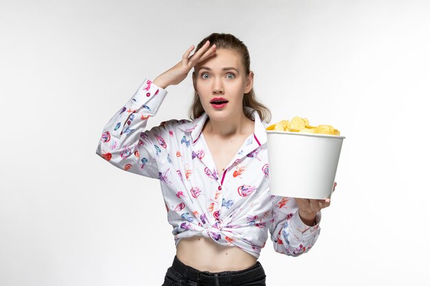 Vue de face jeune femme tenant le panier avec des croustilles regarder un film sur une surface blanche légère