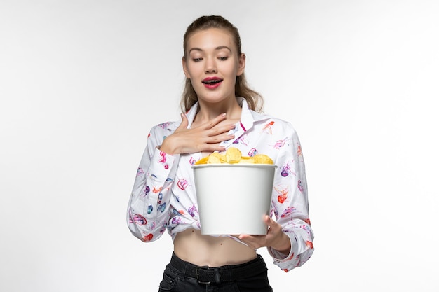 Vue de face jeune femme tenant le panier avec des croustilles sur une surface blanche