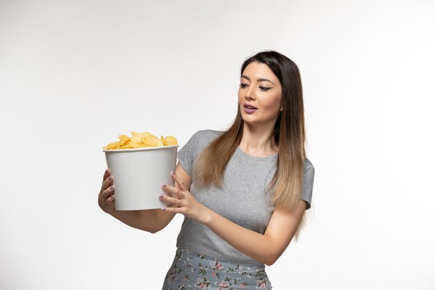 Vue de face jeune femme tenant le panier avec des croustilles sur une surface blanche