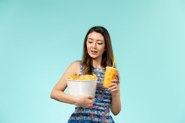 Vue de face jeune femme tenant le panier avec des frites et boire sur un bureau bleu