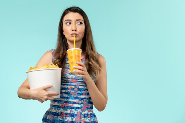 Vue de face jeune femme tenant panier avec frites et boisson sur la surface bleue