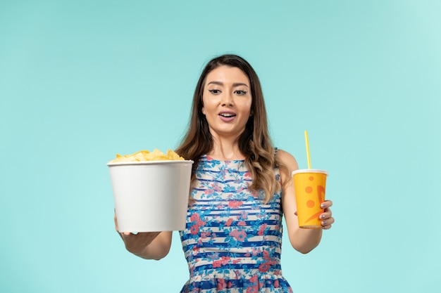 Vue de face jeune femme tenant panier avec frites et boisson sur la surface bleue