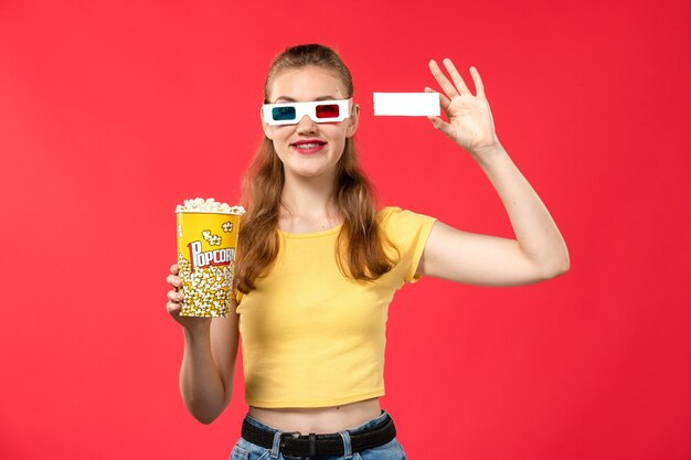 Vue de face jeune femme tenant un paquet de pop-corn et un billet sur le mur rouge clair cinéma cinéma fille film