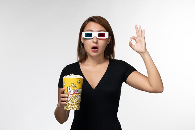 Vue de face jeune femme tenant un paquet de pop-corn dans des lunettes de soleil et regarder un film sur une surface blanche