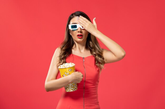 Vue de face jeune femme tenant le paquet de pop-corn en d lunettes de soleil sur le bureau rouge