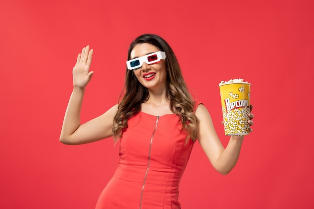 Vue de face jeune femme tenant le paquet de pop-corn en d lunettes de soleil sur le bureau rouge