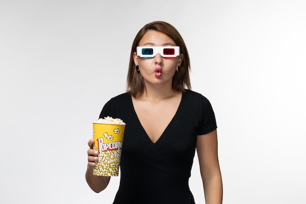 Vue de face jeune femme tenant le paquet de pop-corn en d lunettes de soleil faisant des grimaces sur une surface blanche