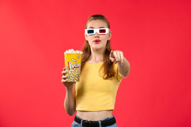 Vue de face jeune femme tenant le paquet de pop-corn en -d lunettes de soleil sur mur rouge clair cinéma cinéma fille film