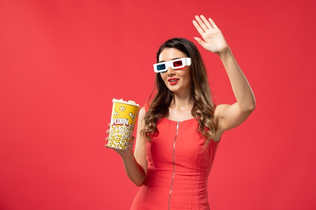 Vue de face jeune femme tenant le paquet de pop-corn en d lunettes de soleil sur la surface rouge