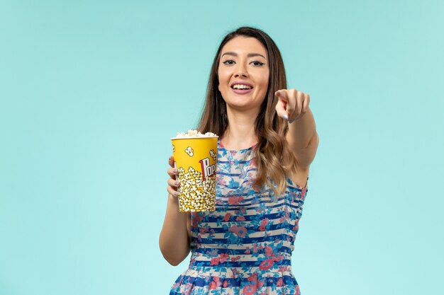 Vue de face jeune femme tenant un paquet de pop-corn regarder un film et rire sur la surface bleue