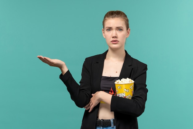 Vue de face jeune femme tenant un paquet de pop-corn regarder un film sur une surface bleu clair