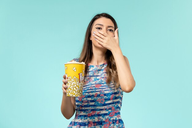 Vue de face jeune femme tenant un paquet de pop-corn regarder un film sur une surface bleue