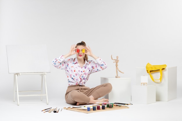 Vue de face jeune femme tenant des peintures colorées à l'intérieur de boîtes sur fond blanc