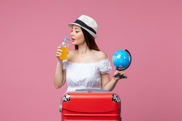 Vue de face jeune femme tenant un petit globe et un cocktail sur le mur rose voyage d'été voyage couleur chaleur vacances