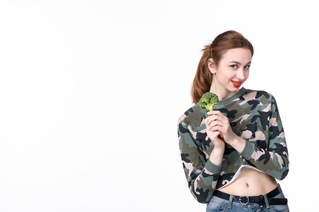 Vue de face jeune femme tenant peu de brocoli vert sur fond blanc déjeuner repas nourriture poids régime soins de santé plat salade