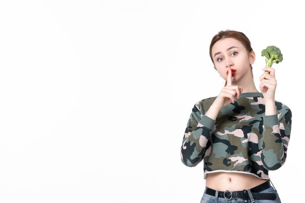 Vue de face jeune femme tenant peu de brocoli vert sur fond blanc repas plat déjeuner santé poids humain santé régime alimentaire