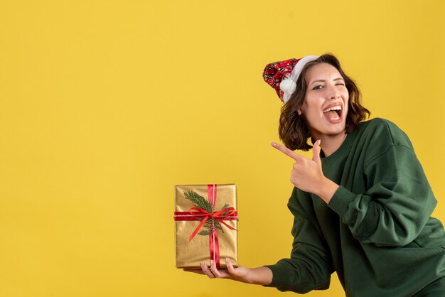 Vue de face de la jeune femme tenant peu de cadeau de Noël sur le mur jaune