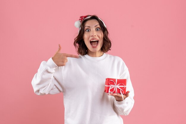 Vue de face de la jeune femme tenant peu de cadeau de Noël sur le mur rose