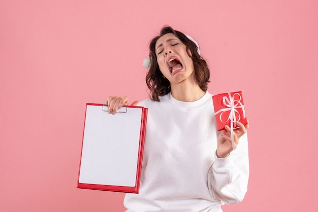 Vue de face de la jeune femme tenant peu de cadeau de Noël et note de dossier sur le mur rose