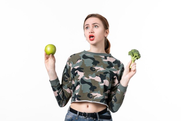 Vue de face jeune femme tenant une pomme verte et peu de brocoli sur fond blanc bien-être de la peau soins de santé horizontaux fruits humains