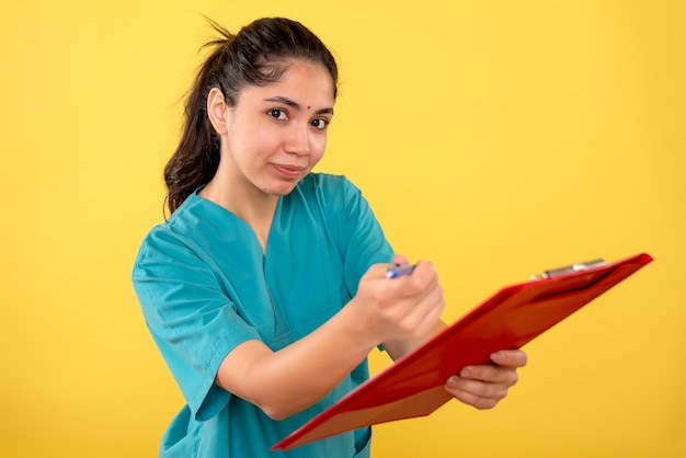 Vue de face de la jeune femme tenant le presse-papiers donnant un stylo sur le mur jaune