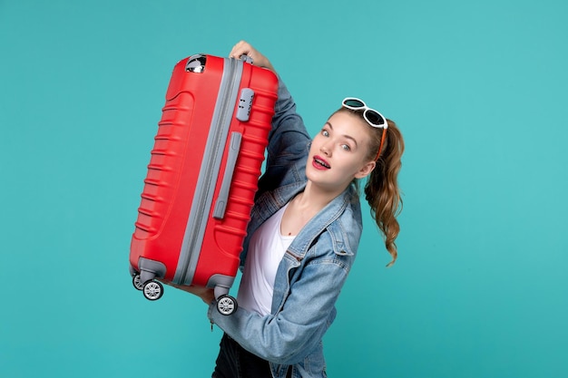 Vue de face jeune femme tenant son sac rouge et se préparant pour le voyage sur le bureau bleu