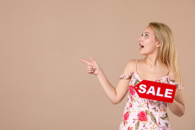 Vue de face d'une jeune femme tenant un tableau de vente rouge sur un mur marron