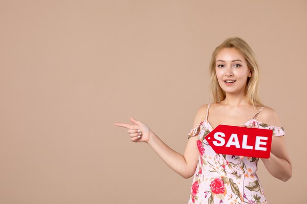 Vue de face d'une jeune femme tenant un tableau de vente rouge sur un mur marron