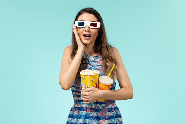 Vue de face jeune femme tenant un verre de maïs soufflé dans des lunettes de soleil sur la surface bleue