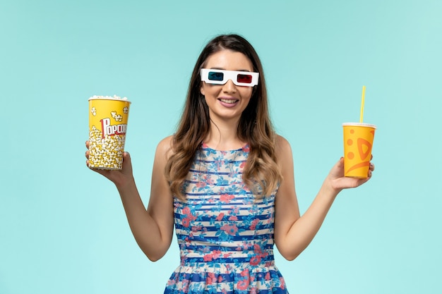 Vue de face jeune femme tenant un verre de maïs soufflé dans des lunettes de soleil sur la surface bleue