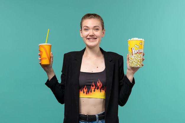 Vue de face jeune femme tenant un verre de pop-corn et regarder un film sur un bureau bleu