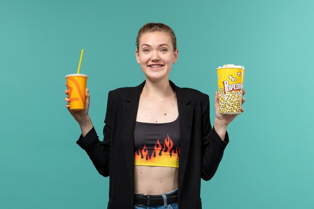 Vue de face jeune femme tenant un verre de pop-corn et regarder un film sur un bureau bleu