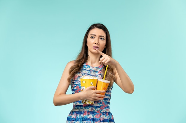 Vue de face jeune femme tenant un verre de pop-corn et regarder un film sur la surface bleue