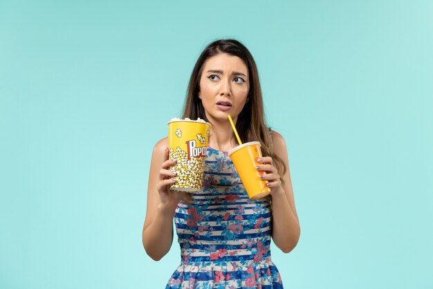 Vue de face jeune femme tenant un verre de pop-corn et regarder un film sur la surface bleue