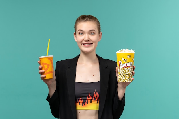 Vue de face jeune femme tenant un verre de pop-corn et regarder un film sur la surface bleue