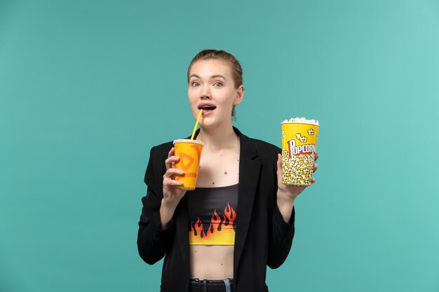 Vue de face jeune femme tenant un verre de pop-corn et regarder un film sur la surface bleue