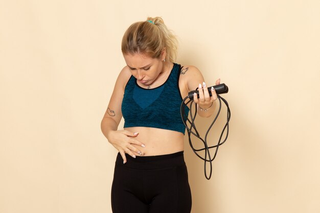 Vue de face jeune femme en tenue de sport tenant des cordes à sauter sur un mur blanc santé entraînement corps sport beauté exercices