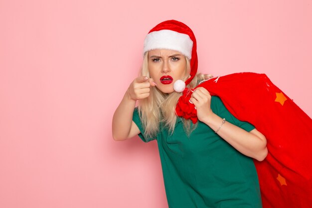 Vue de face jeune femme transportant un sac rouge avec des cadeaux sur le modèle de mur rose Noël nouvel an photo vacances santa