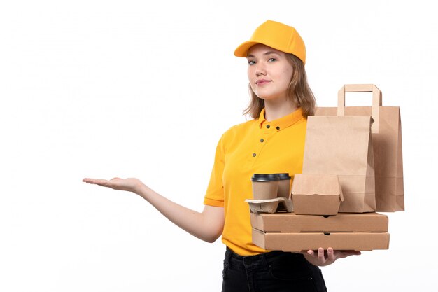 Une vue de face jeune femme travailleur de messagerie de service de livraison de nourriture tenant des boîtes de pizza paquets alimentaires et tasses à café souriant sur blanc