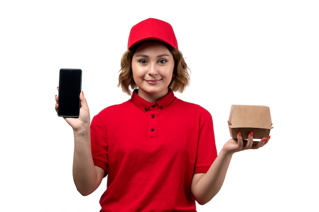 Une vue de face jeune femme travailleur de messagerie de service de livraison de nourriture tenant le paquet de livraison de nourriture et smartphone sur blanc